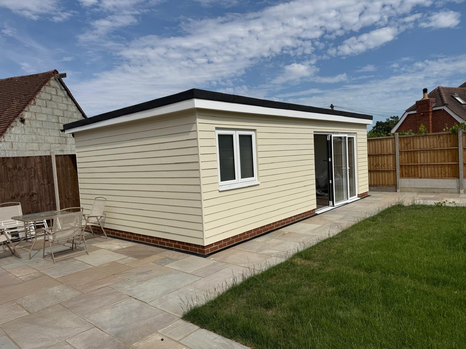 Cream weatherboarded garden annexe with a flat roof and sliding doors