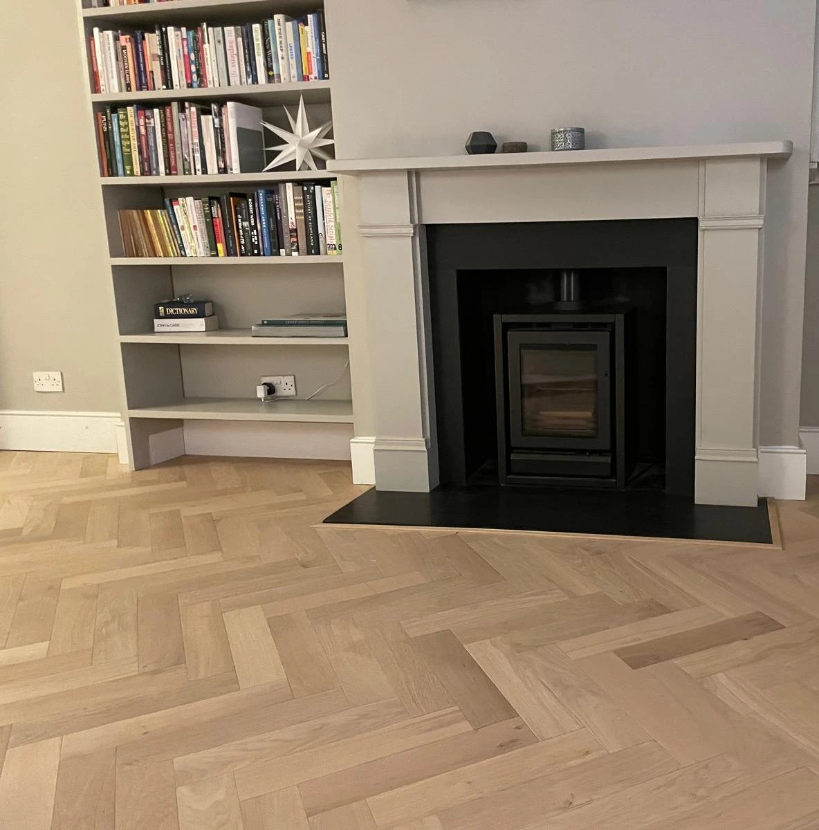Light oak herringbone floor laid around a stone hearth and wood burner