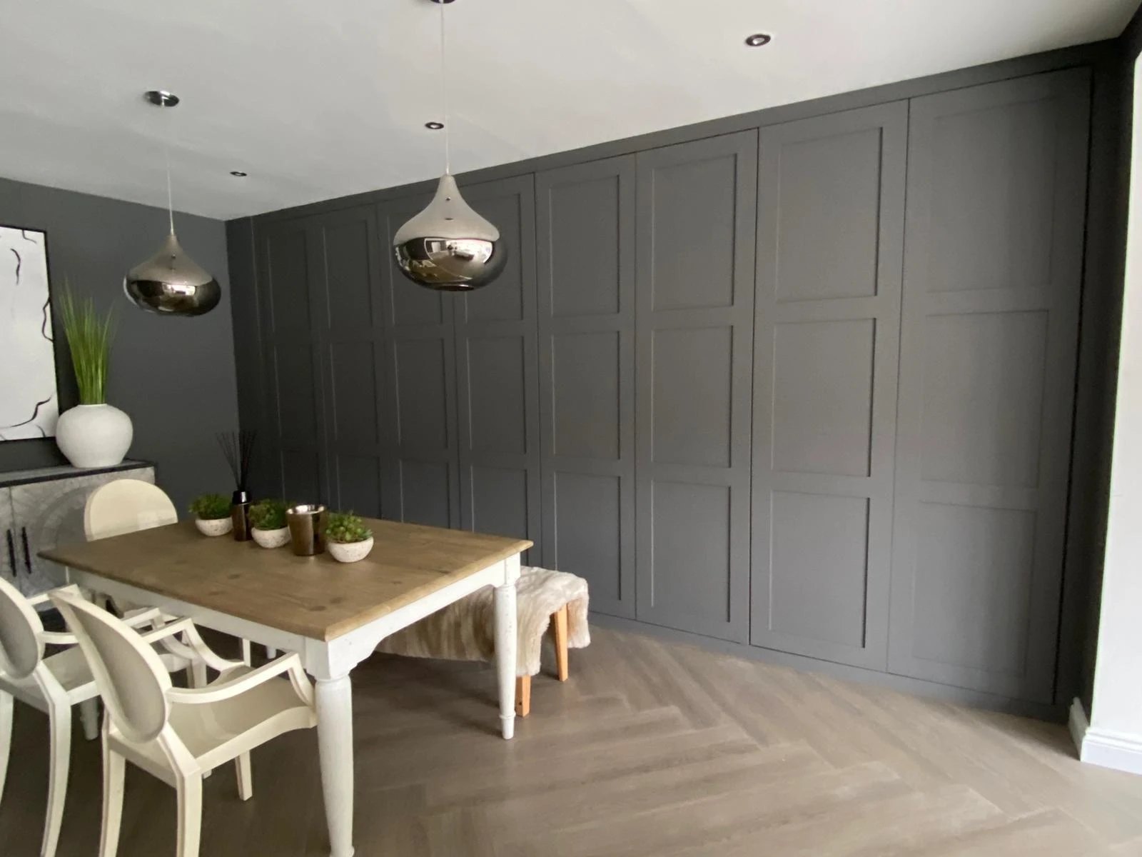 Wall of panelled wardrobe doors painted dark grey in a dining room